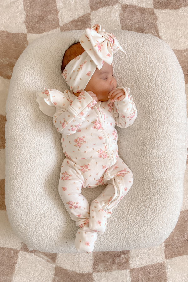 Baby lying in a baby nest wearing the onesie with a matching headband. Frilly Sleeve Zip Onesie in Skyla by Skylaroseco