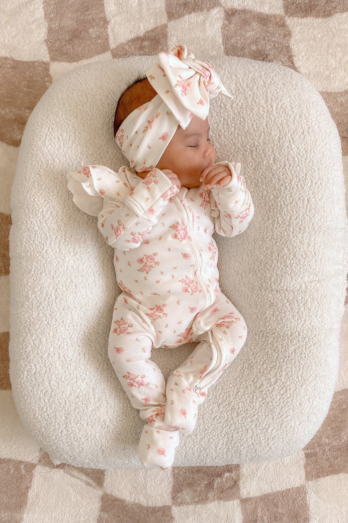 Baby lying in a baby nest wearing the onesie with a matching headband. Frilly Sleeve Zip Onesie in Skyla by Skylaroseco