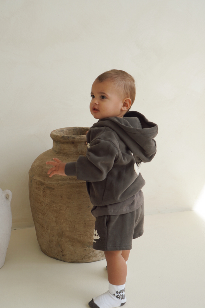 Toddler standing by a clay vase in the charcoal hoodie and shorts set. Love & Leisure Kids Lounge Set in Moondust by Skylaroseco