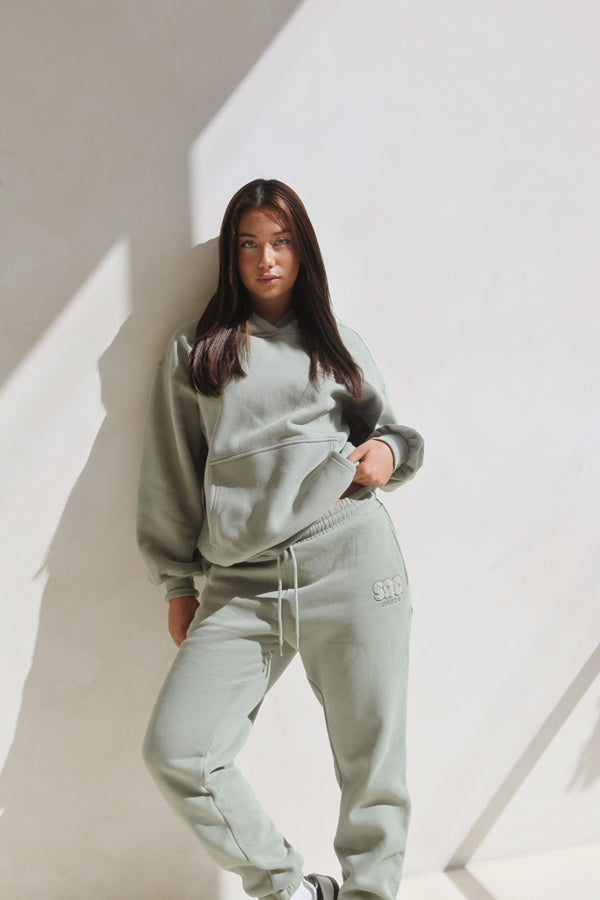 Woman standing in the sage hoodie and sweatpants set. Cosy Club 2.0 Adults Sweatpants in Sage by Skylaroseco
