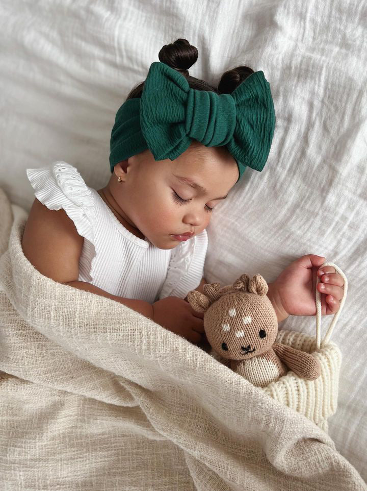 Beautiful little girl wearing an emerald green oversized bow headband while sleeping 