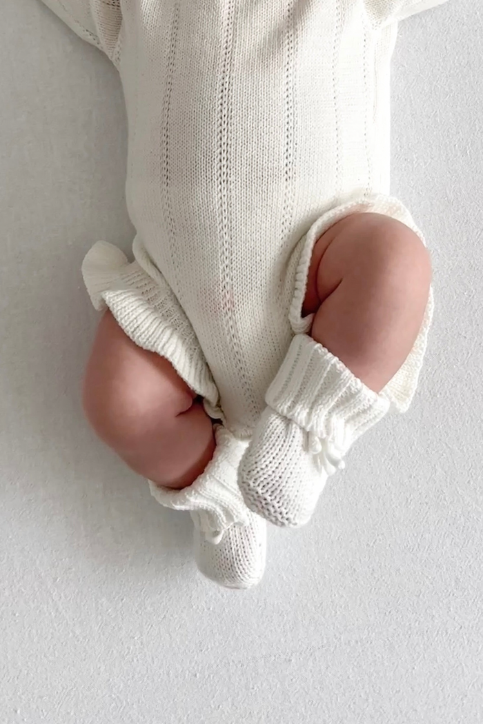 Close-up of a baby's legs wearing the booties. Knitted Booties in White by Skylaroseco
