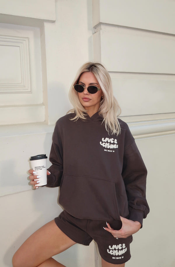 Woman in sunglasses wearing the charcoal hoodie and lounge shorts, holding a coffee. Love & Leisure Adults Hoodie in Moondust by Skylaroseco