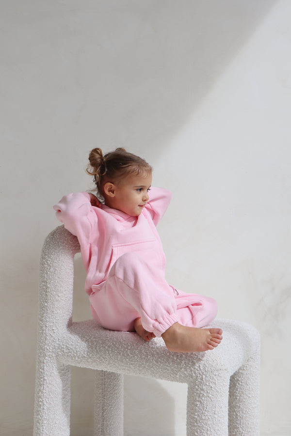 Toddler sitting on a white chair wearing the pink lounge set. Cosy Club 2.0 Kids Lounge Set in Pink by Skylaroseco