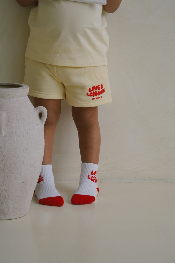 Close-up of a child wearing the socks with cream lounge shorts. Love & Leisure Kids Socks in Cherry by Skylaroseco