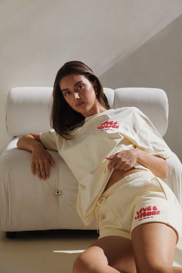 Woman reclining on a white sofa in the cream lounge shorts and tee. Love & Leisure Adults Lounge Shorts in Cherry Cream by Skylaroseco