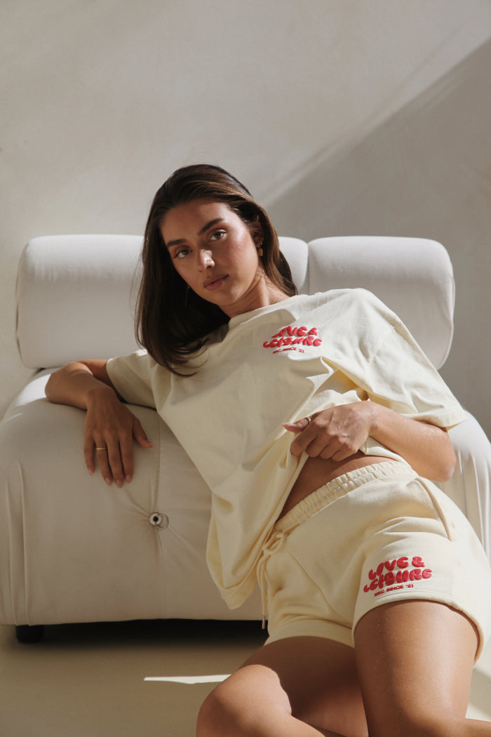 Woman reclining on a white sofa in the cream lounge shorts and tee. Love & Leisure Adults Lounge Shorts in Cherry Cream by Skylaroseco