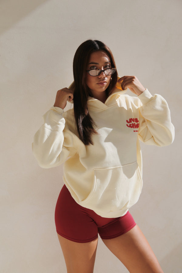 Woman wearing the cream hoodie with red puff print and red bike shorts. Love & Leisure Adults Hoodie in Cherry Cream by Skylaroseco